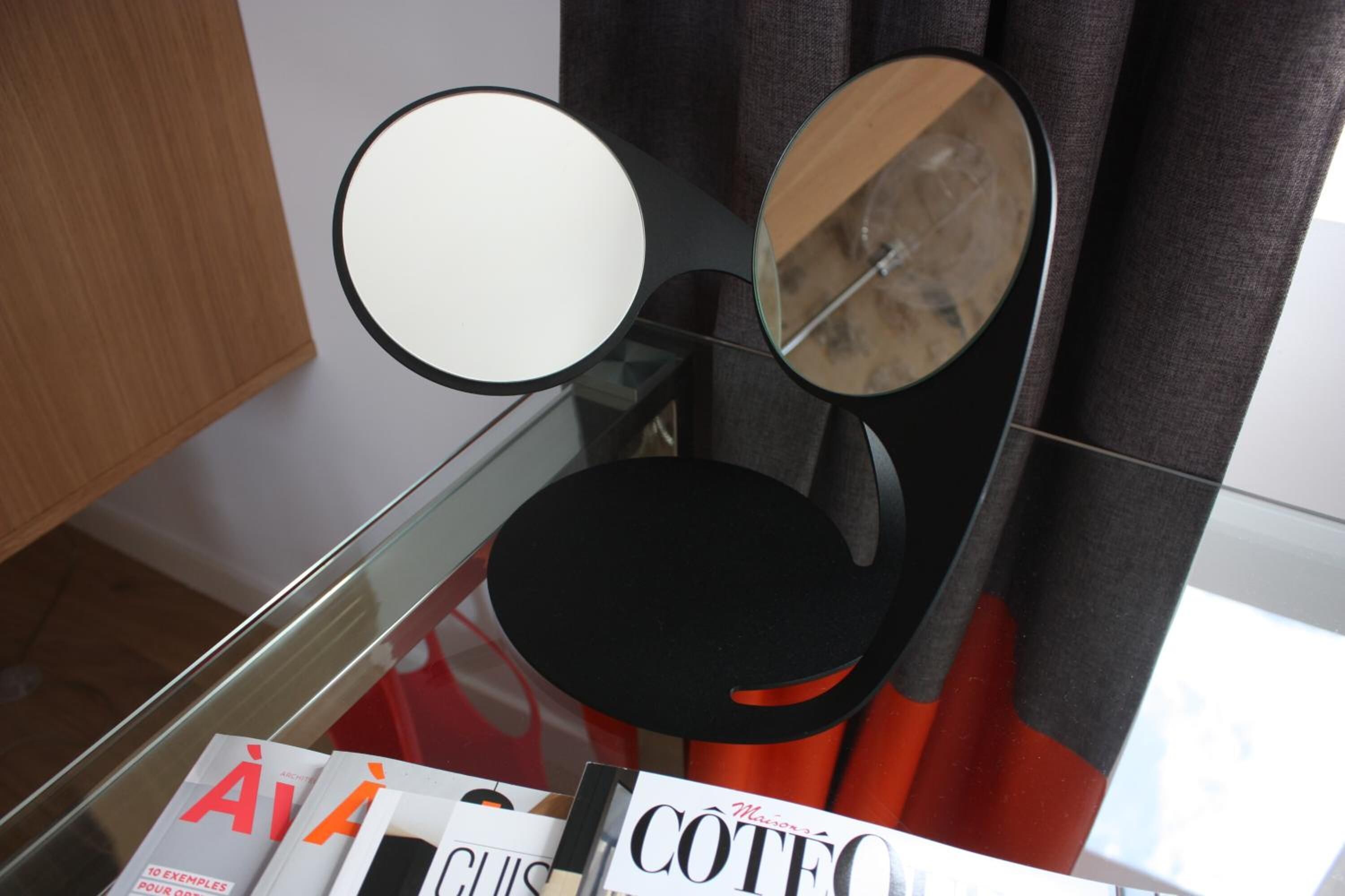 Un interno moderno con un tavolo in vetro che espone riviste e una sedia nera con uno specchio.