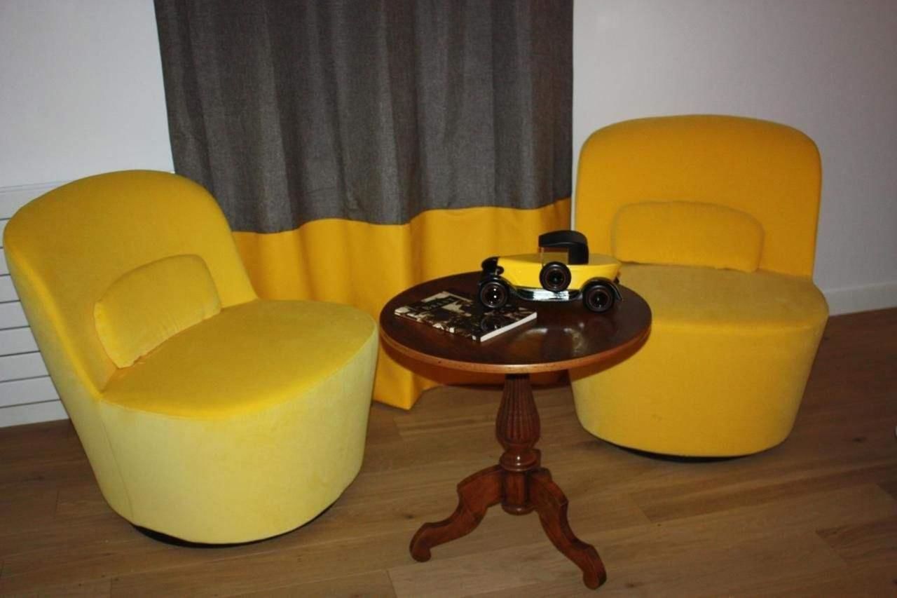 Een kamer met twee gele fauteuils en een kleine houten tafel met een camera en een boek.