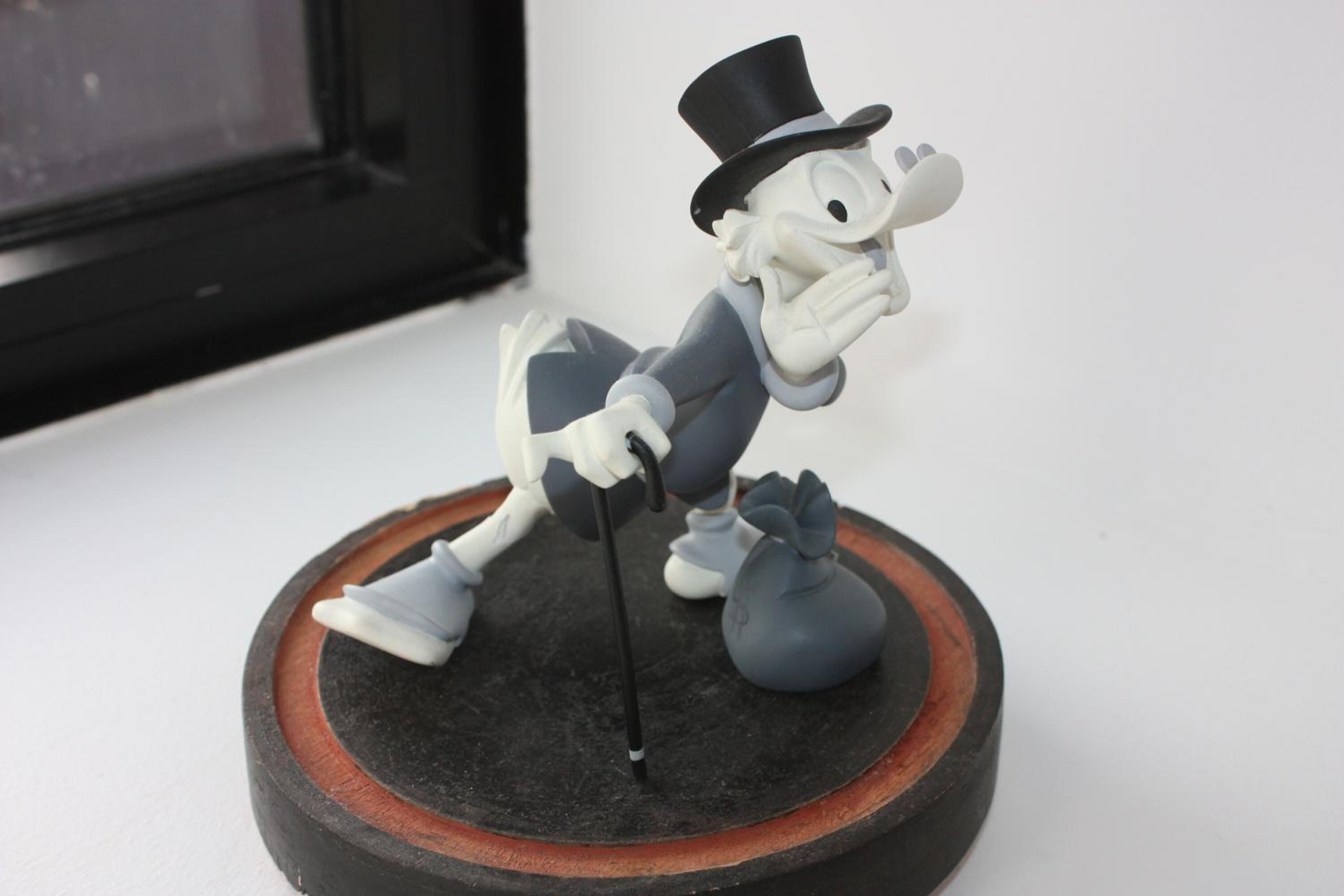 Uma figura de um personagem com chapéu alto e bengala, em pé sobre uma base circular com borda vermelha e preta.