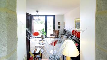 Ein modernes Wohnzimmer mit einem roten Sofa, einem Couchtisch und einer Lampe. Eine Tür führt zu einem Balkon mit Blick auf Grünflächen.