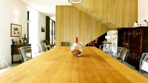 Une longue table à manger en bois, agrémentée d’un vase en verre servant de centre de table, et entourée de chaises transparentes.