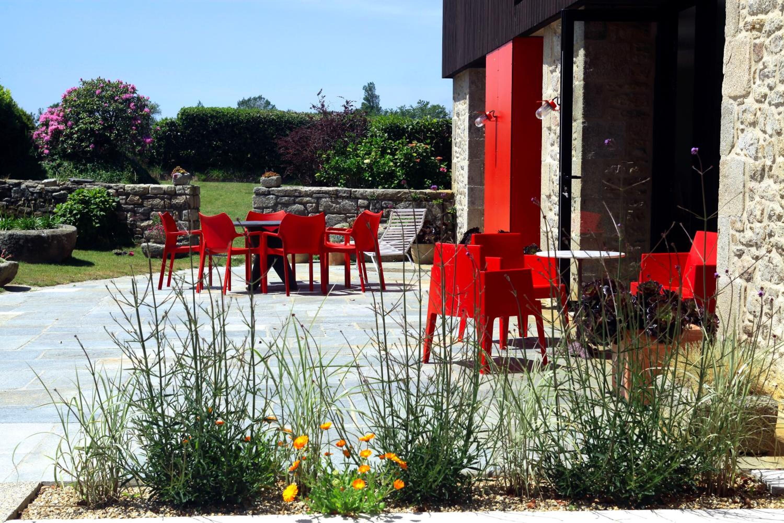 An outdoor patio with red chairs and tables, surrounded by stone walls and greenery.