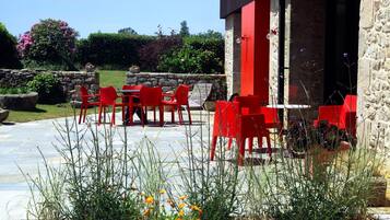 An outdoor patio with red chairs and tables, surrounded by stone walls and greenery.