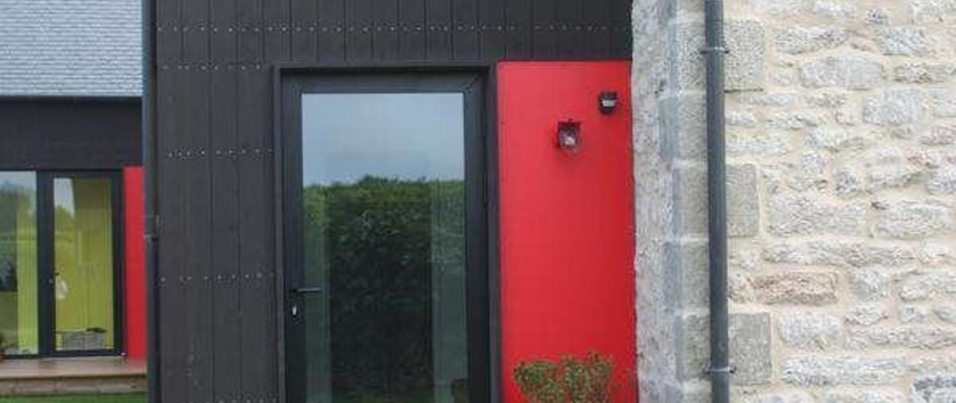 Un bâtiment moderne doté d’une façade sombre et d’un mur d’accent de couleur rouge.