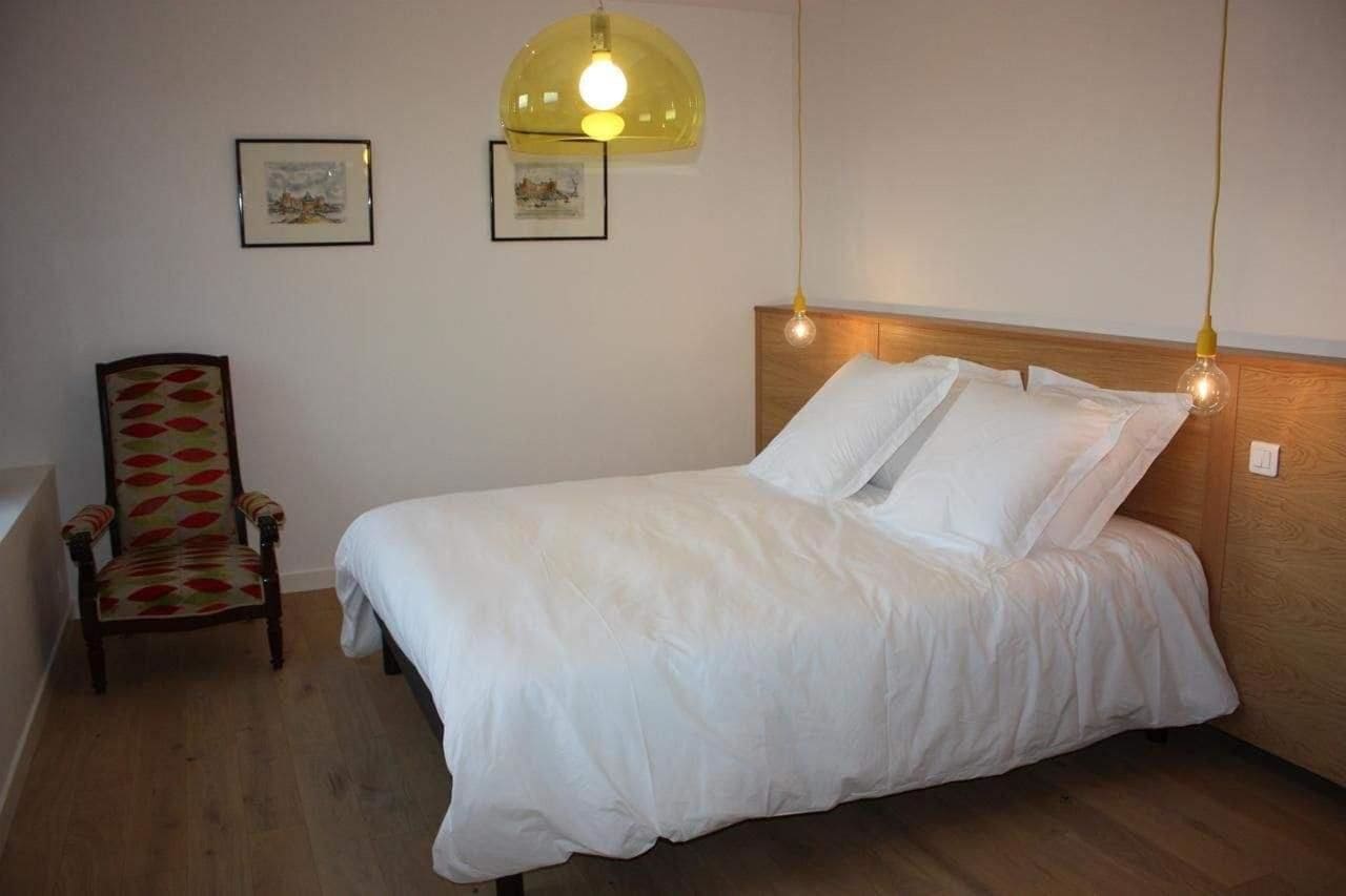 A neatly made bed with white linens, a wooden headboard, and two wall-mounted light fixtures.