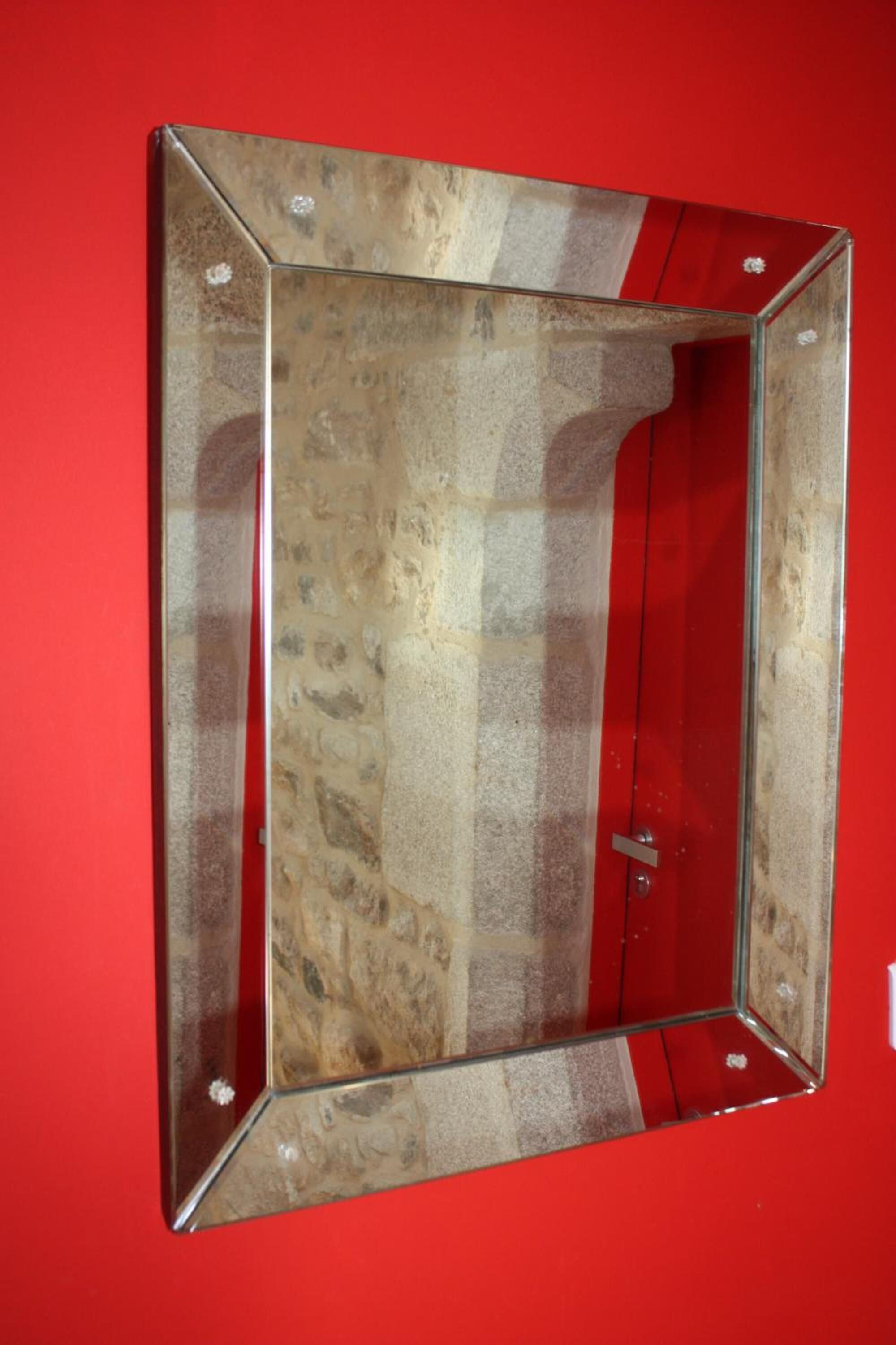 Un miroir avec un cadre qui ressemble à de la pierre, fixé sur un mur rouge.