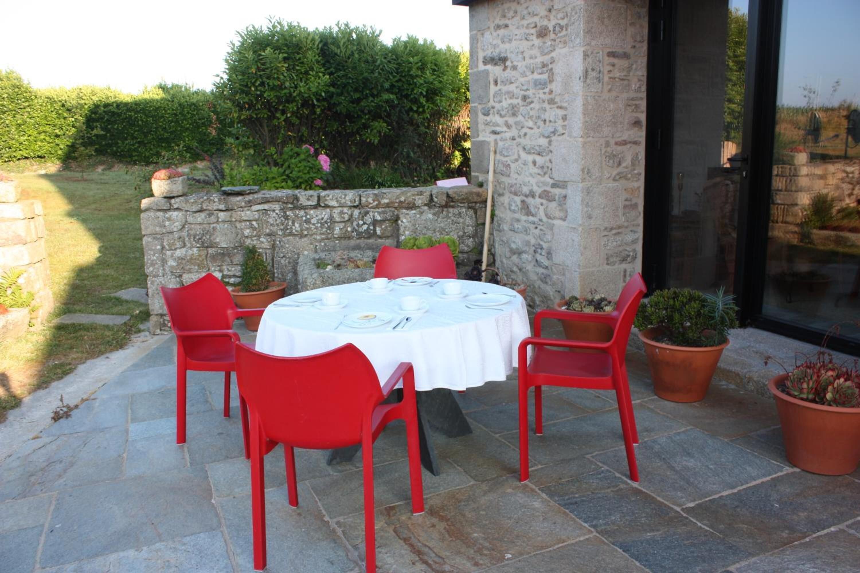 Un patio de piedra con una mesa redonda dispuesta para cuatro personas, rodeado de sillas rojas.