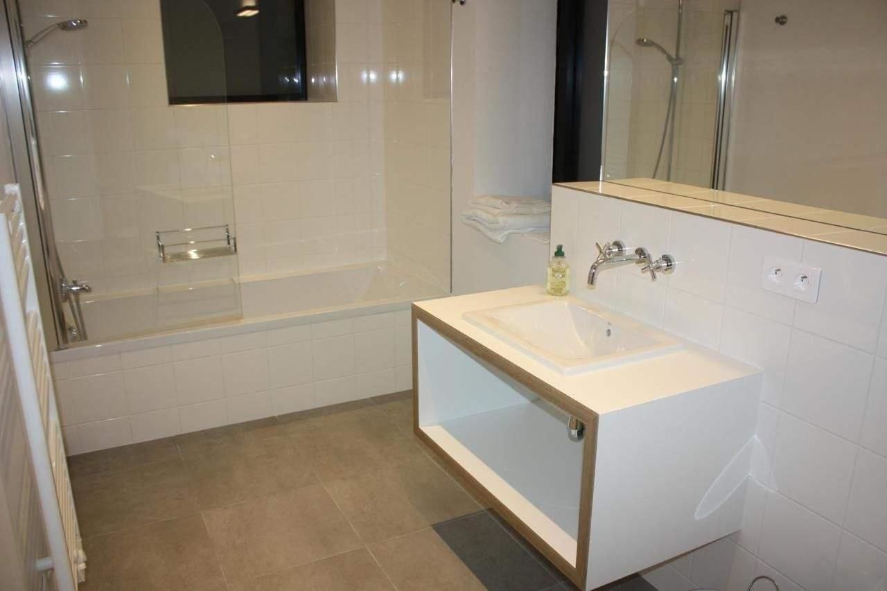 Een moderne badkamer met een douchecabine van glas, een witte wastafel en een spiegel erboven.