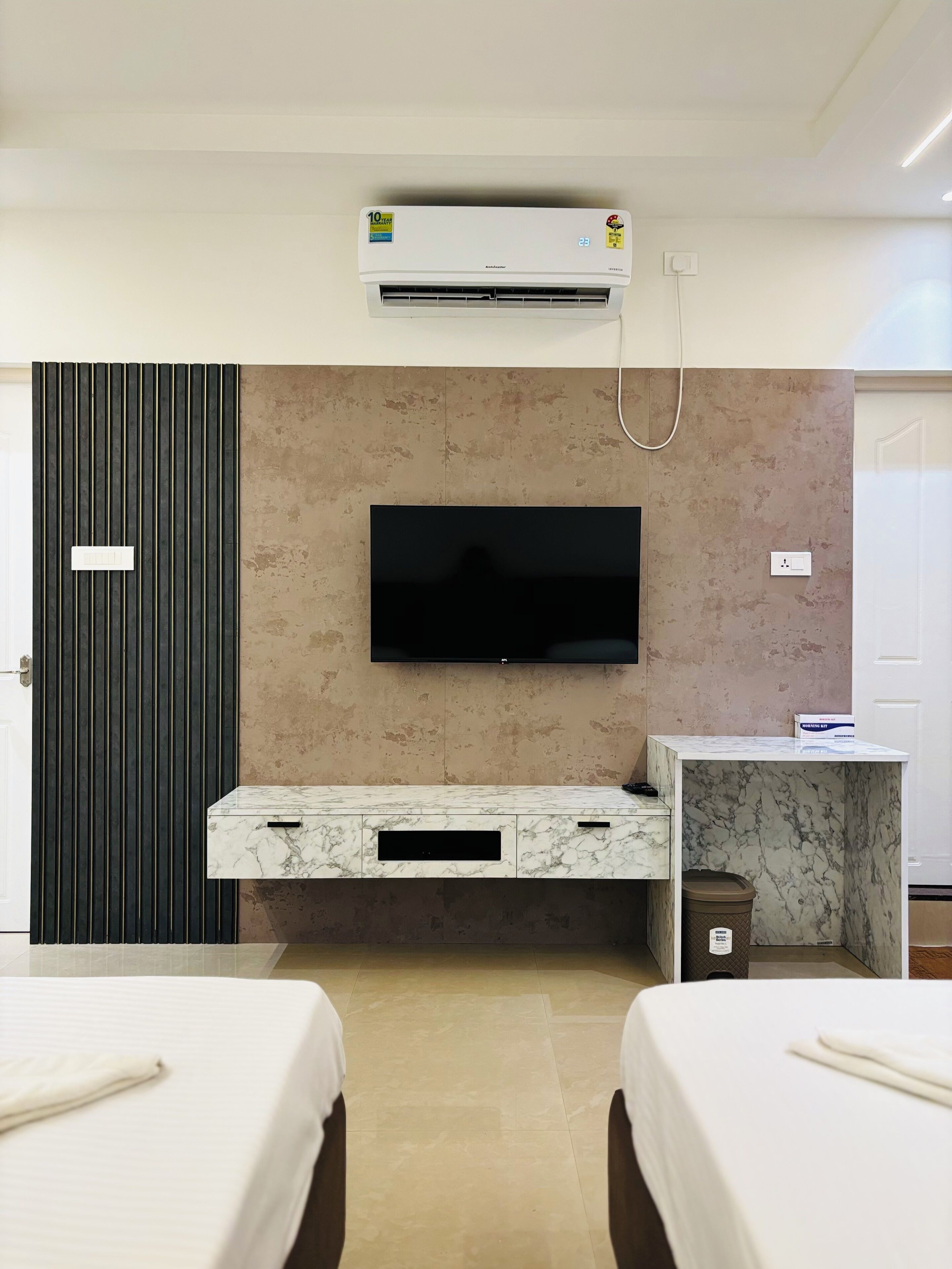 A hotel room with a flat-screen TV mounted on a marble console, a wall-mounted air conditioner, and a door with a light switch.