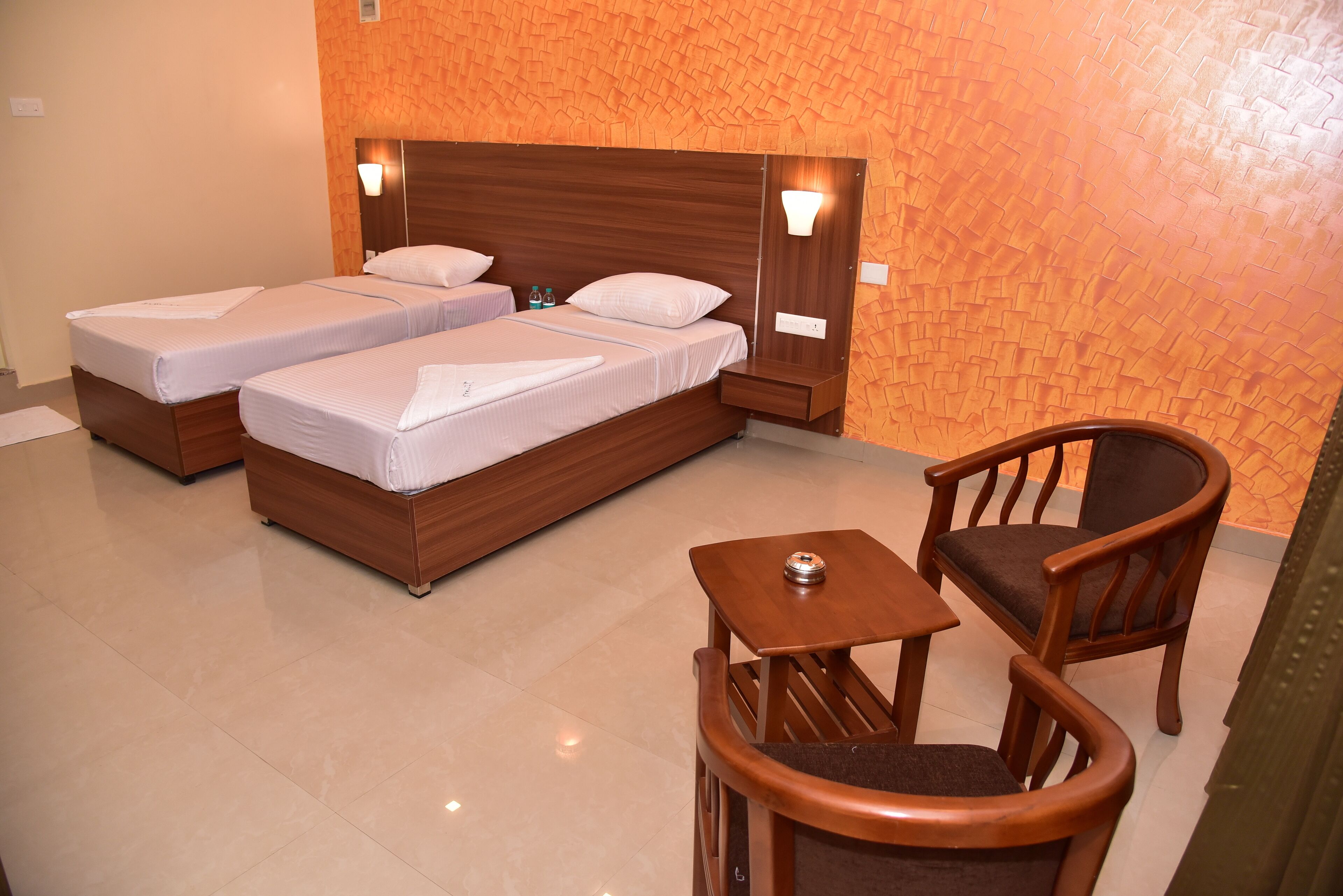 Habitación de hotel con dos camas individuales, una mesita de madera, una silla y una mesita de noche.