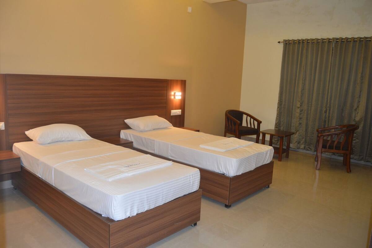 Una habitación de hotel con dos camas de madera, una mesita de noche, una silla y una pequeña mesa.