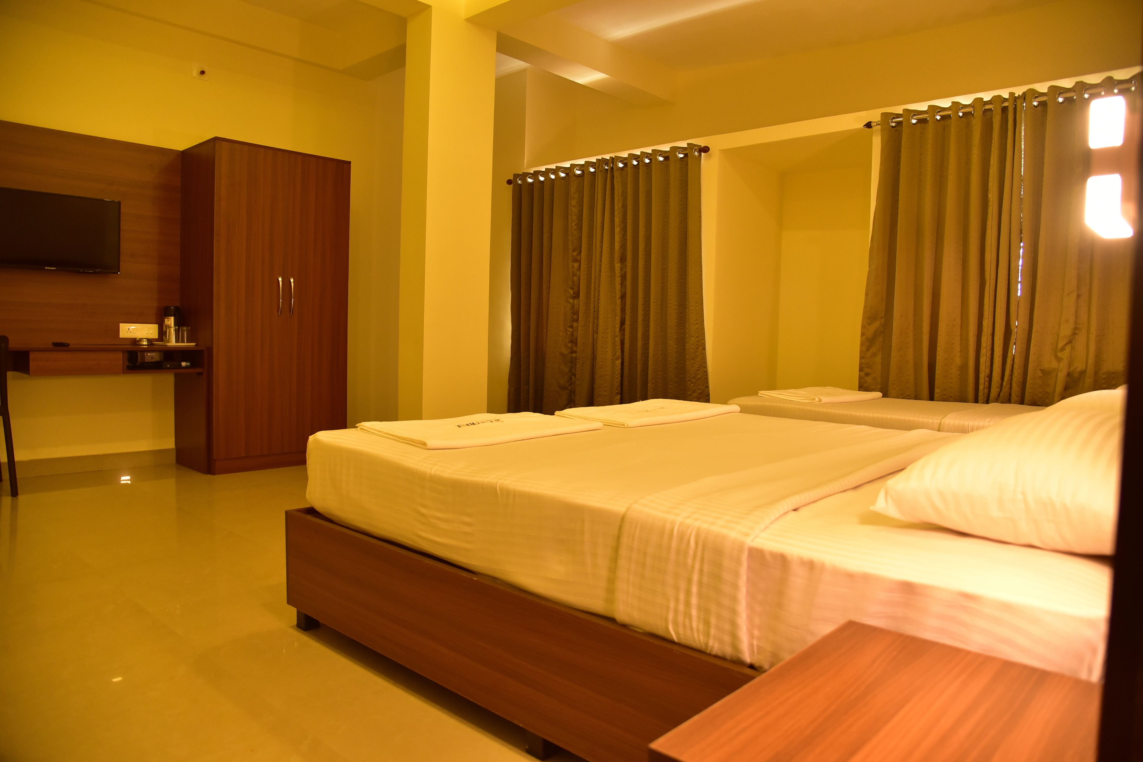A hotel room with a bed, a wooden wardrobe, a desk with a flat-screen TV, and a bathroom with curtains.