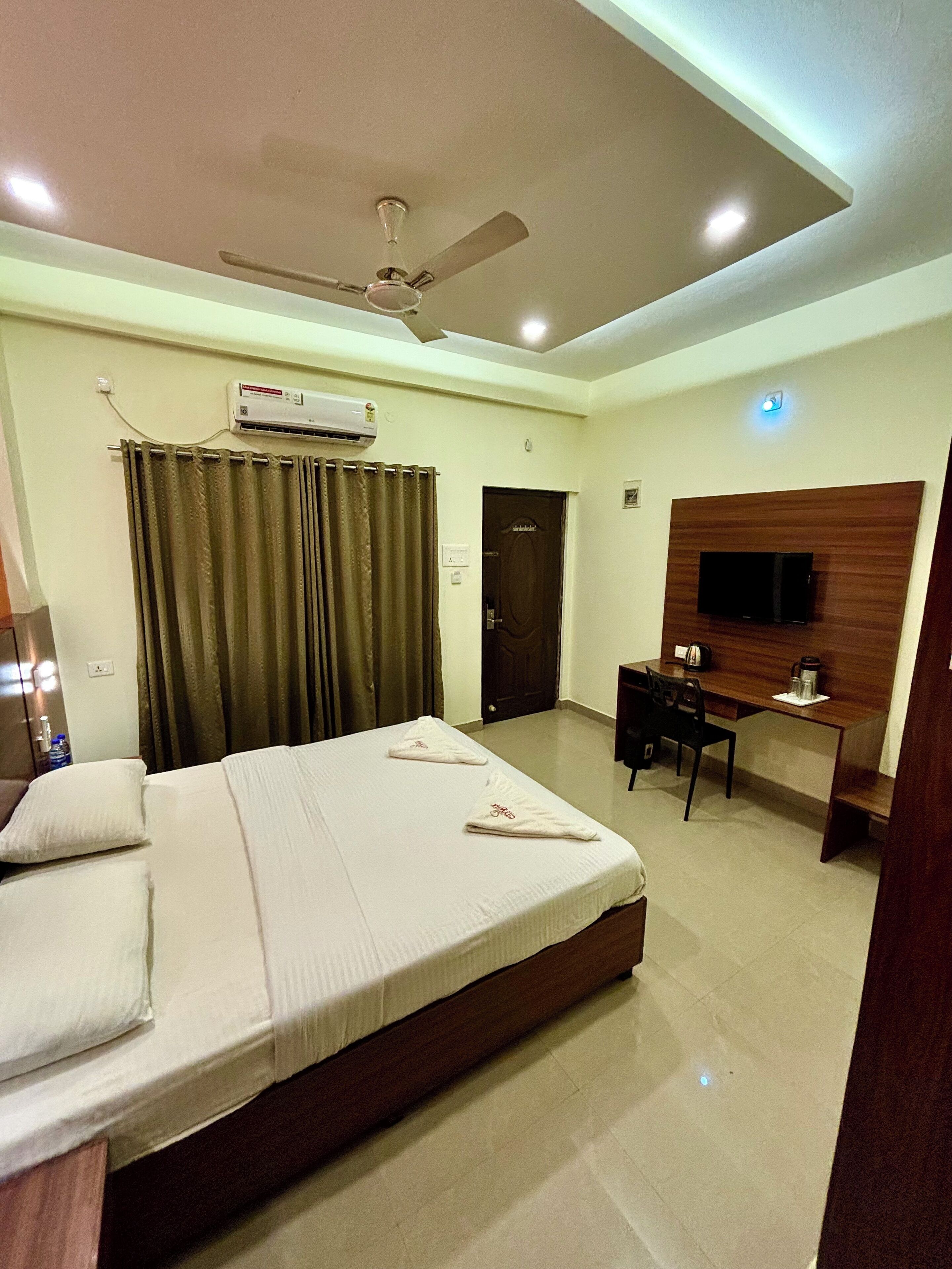 A hotel room with a bed, a desk, a chair, a television, and an air conditioning unit.