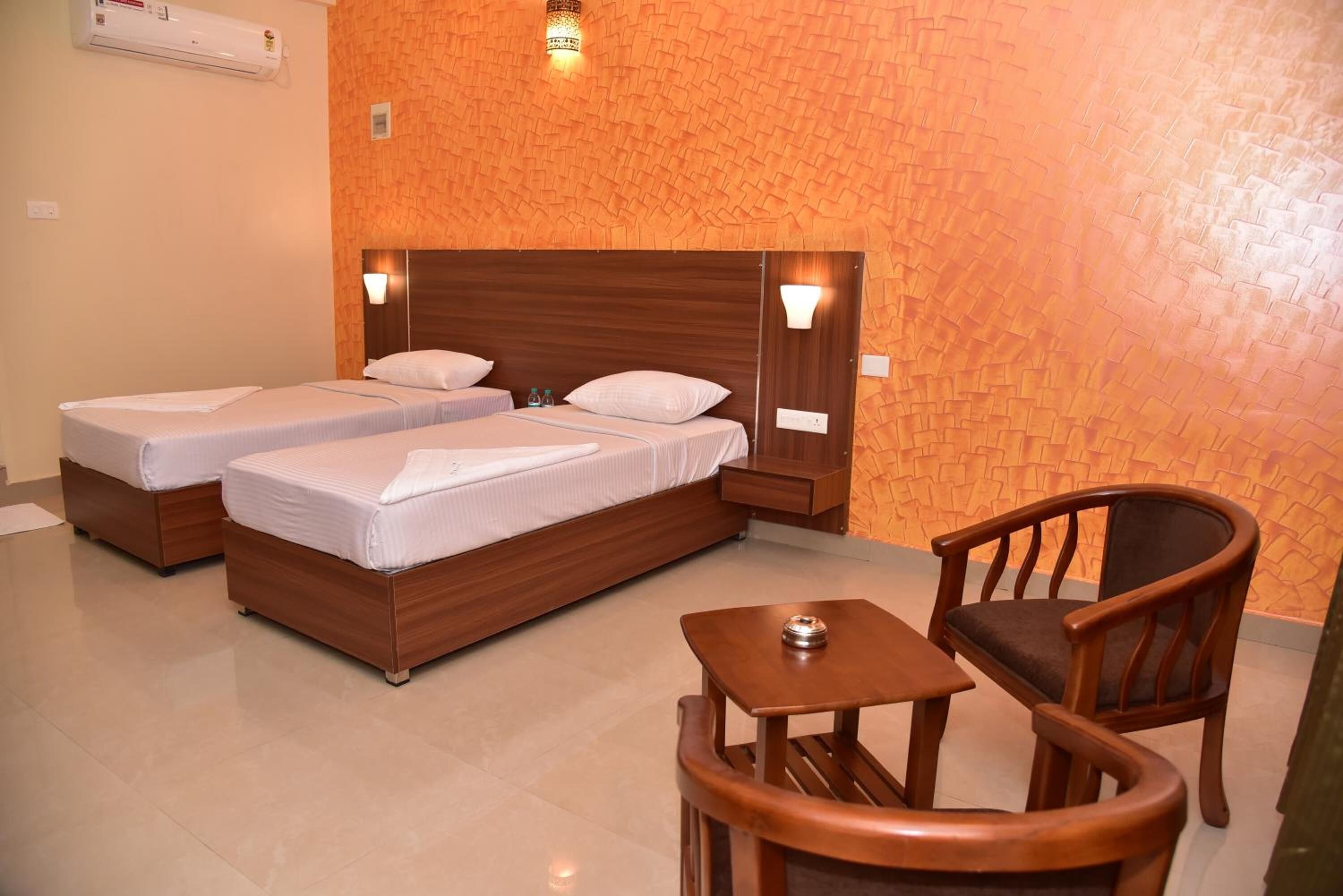 A hotel room with two beds, a wooden headboard, a small table, and a chair.