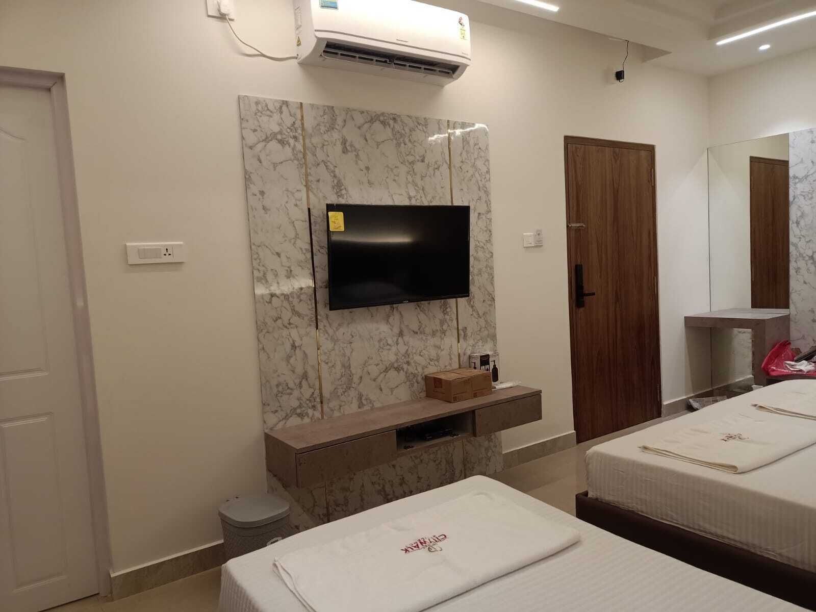 A hotel room with a marble wall, a flat-screen TV, a wooden cabinet, a wooden door, and two beds with white linens.