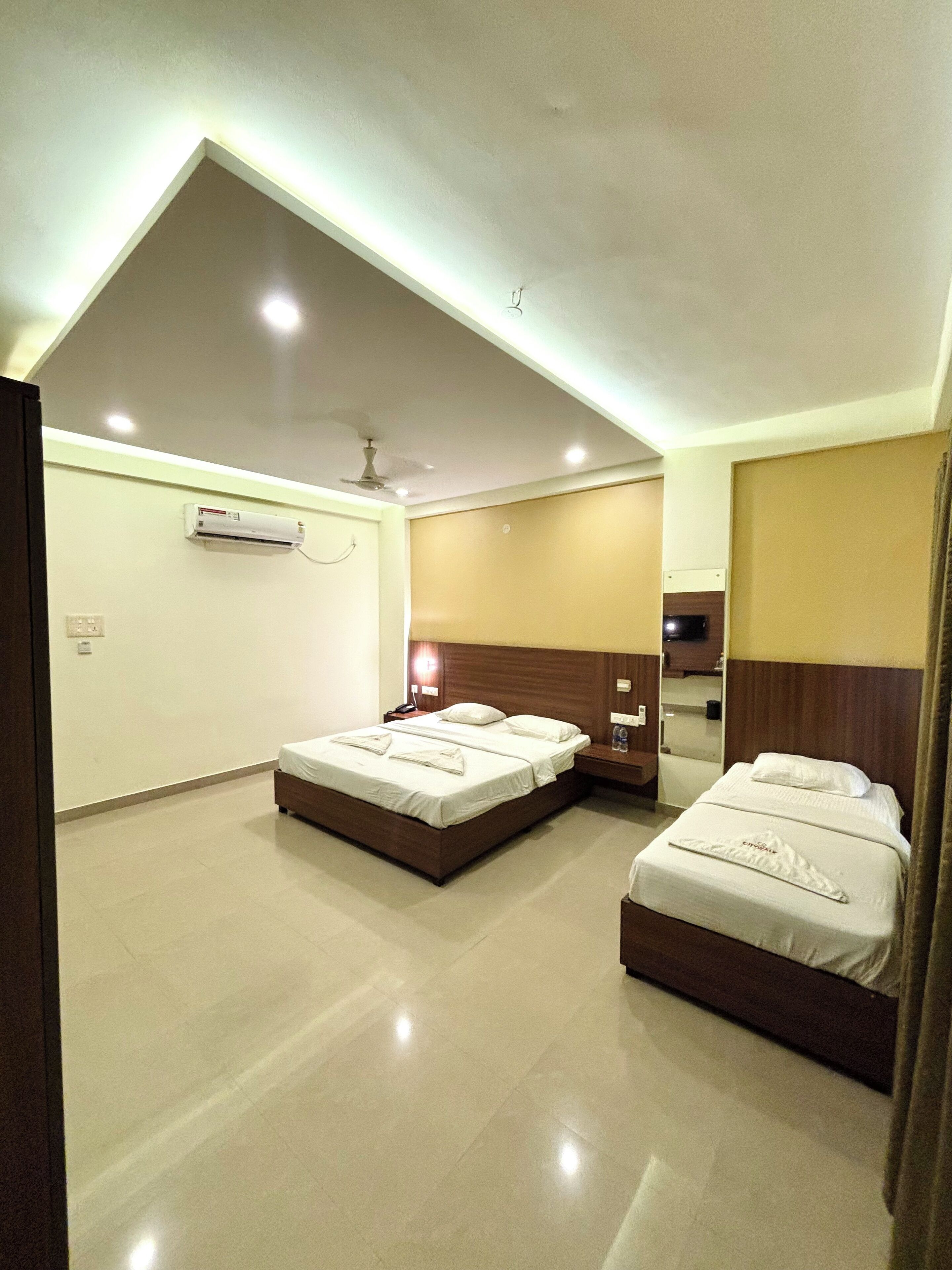 A hotel room with two beds, a ceiling fan, an air conditioning unit, and a mirror.