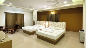 Quarto de hotel com duas camas, uma escrivaninha, cadeiras, ventilador de teto e uma janela grande.