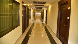 Corredor de hotel com portas em ambos os lados, chão em mosaico e teto com painéis decorativos.