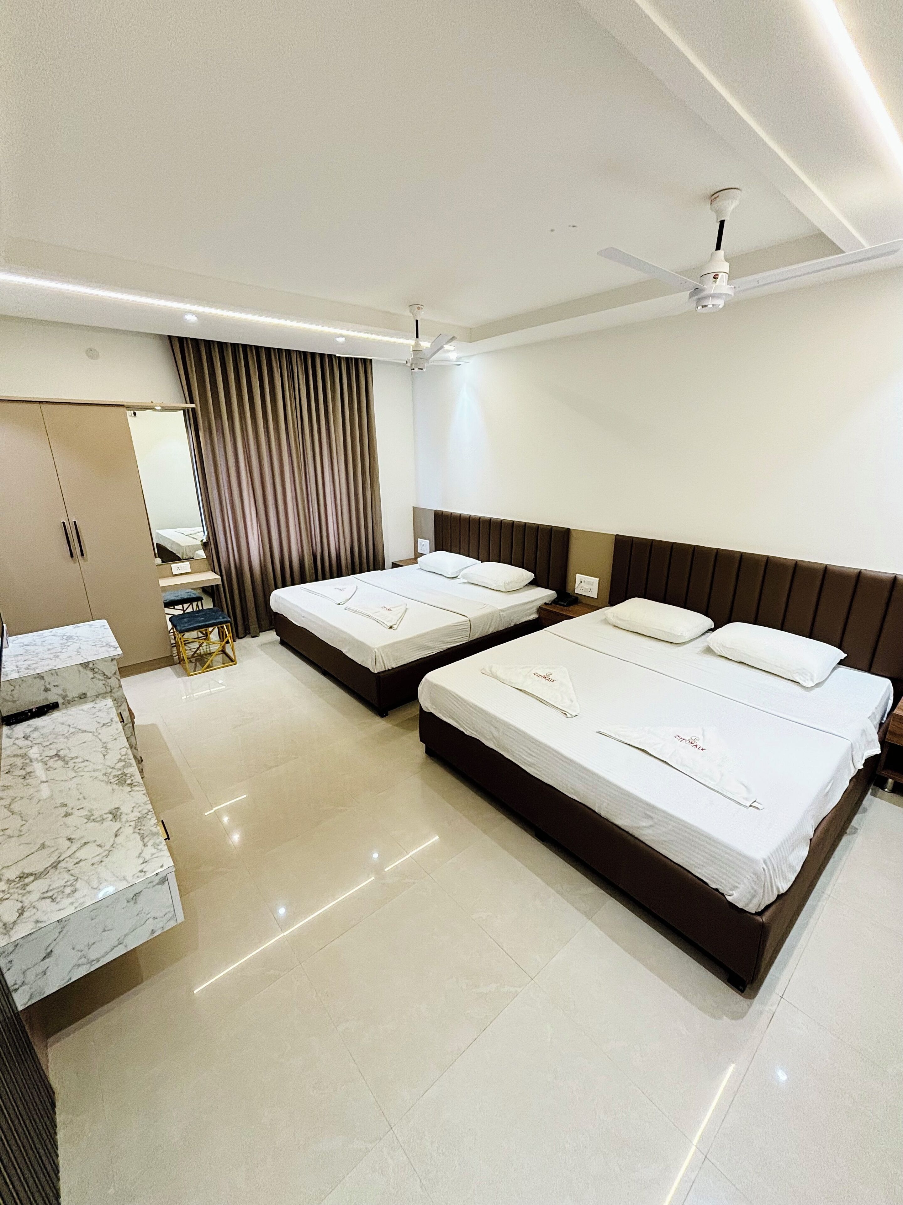 Ein Hotelzimmer mit zwei Betten, einer Marmorwaschtischplatte, einem Kleiderschrank und einem Deckenventilator.