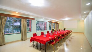Un salón de conferencias con una larga mesa, sillas rojas y ventanas amplias con cortinas.