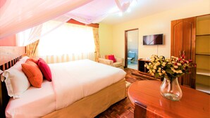 Una habitación de hotel con cama, televisión, una mesa de madera y un jarrón con flores.