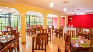 Un restaurante con mesas y sillas de madera, ventanas amplias y una pared de acento en rojo.