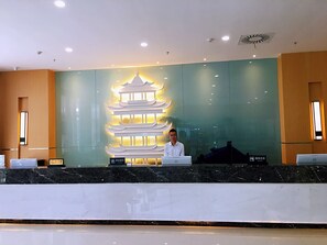 Un mostrador de recepción de diseño moderno, con una pared decorativa que presenta una estructura similar a una pagoda y una pantalla digital que muestra información.