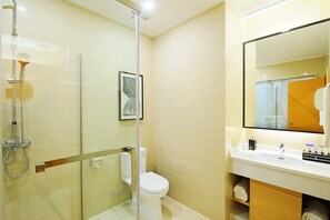 Un baño moderno con cabina de ducha de vidrio, inodoro, lavamanos con espejo y un cuadro enmarcado en la pared.