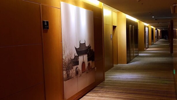 Un pasillo de hotel con paneles de madera, piso alfombrado y una obra de arte en la pared que representa un edificio tradicional.