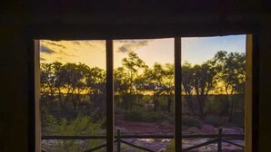 A room with a large window overlooking a natural landscape with trees and a clear sky. - Man Eaters Lodge (Tsavo)