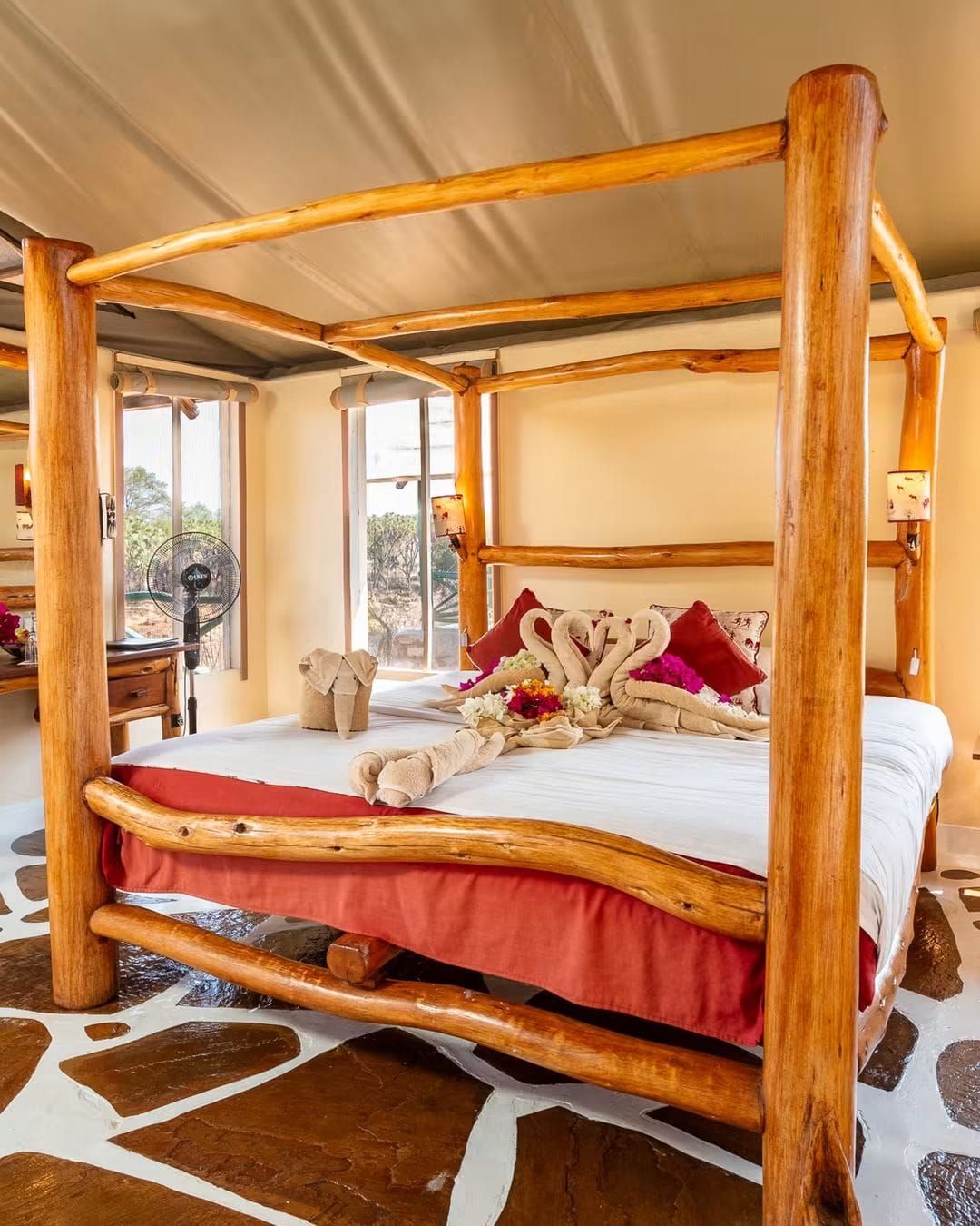 Una cama con dosel de madera, colcha roja y almohadones decorativos.