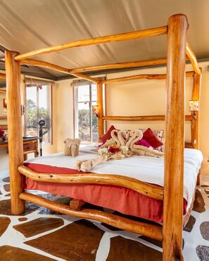 A four-poster bed with a wooden frame, a red bedspread, and decorative pillows. - Man Eaters Lodge (Tsavo)