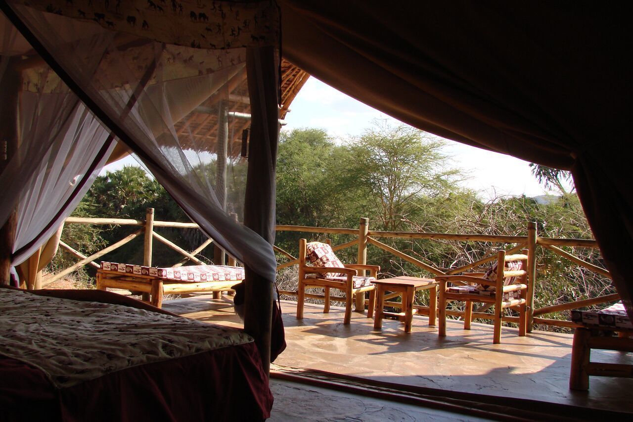 A tent with a bed, a table, and chairs on an outdoor deck with a view of trees.