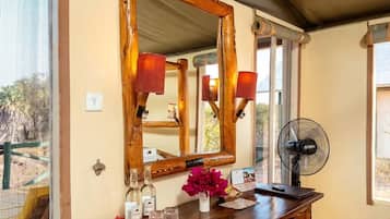 A wooden vanity with a mirror, a fan, and a small table with bottles and a vase of flowers.