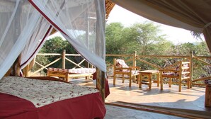 A bedroom with a bed, a canopy, and a balcony with wooden furniture. - Man Eaters Lodge (Tsavo)
