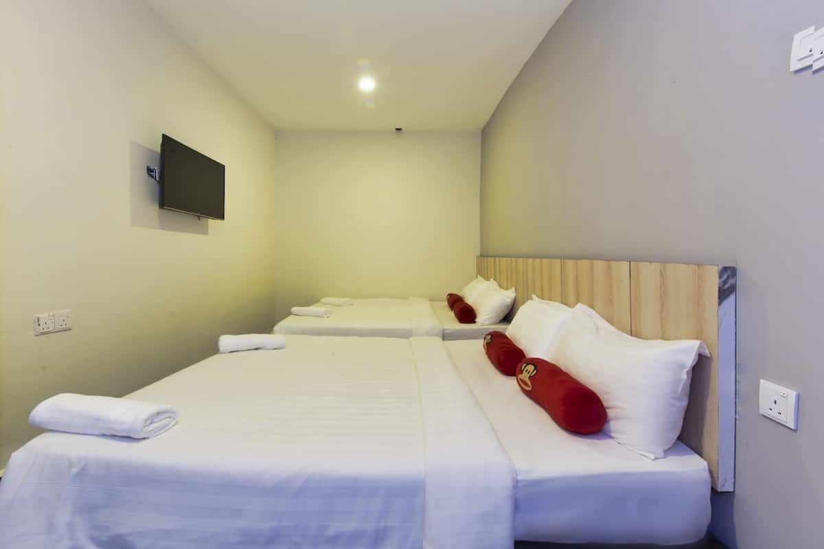 A hotel room with two beds, white bedding, red pillows, a flat-screen TV on the wall, and a wooden headboard.