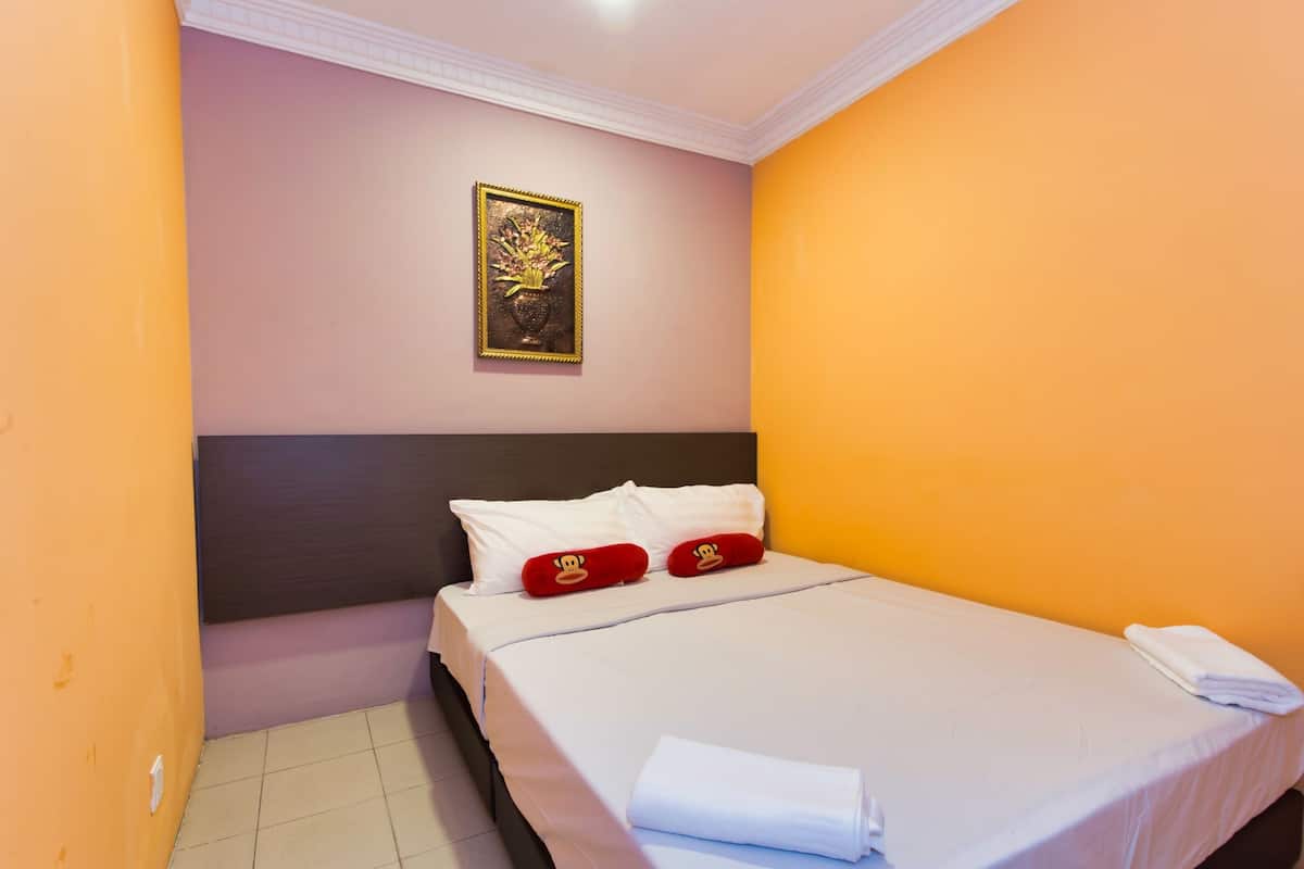 A neatly made bed with white linens and red pillows, a framed picture on the wall, and orange walls.
