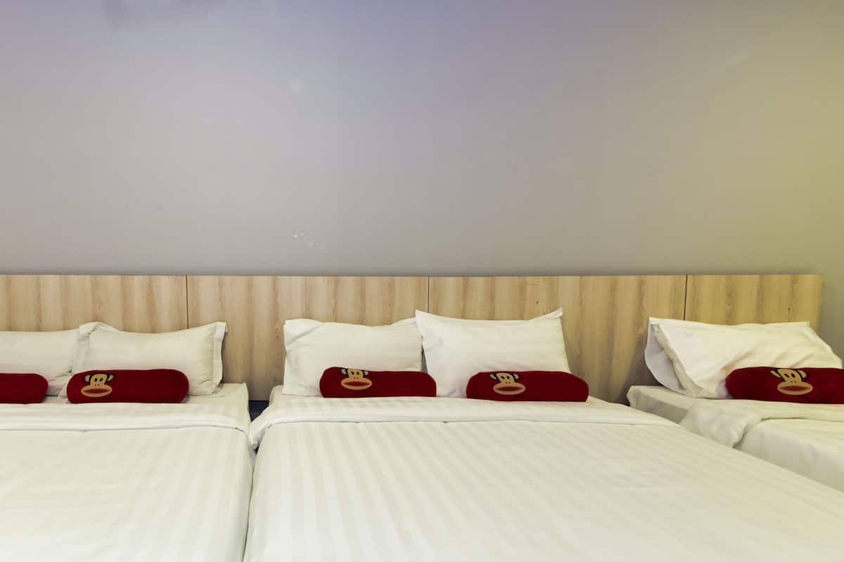 A hotel room with three beds, each with white bedding and red pillows with a monkey design.