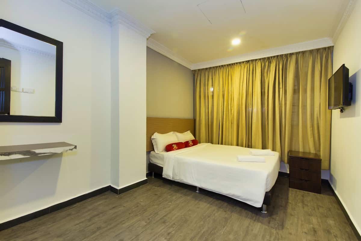 A hotel room with a bed, a bedside table, a mirror, a television, and a window with curtains.