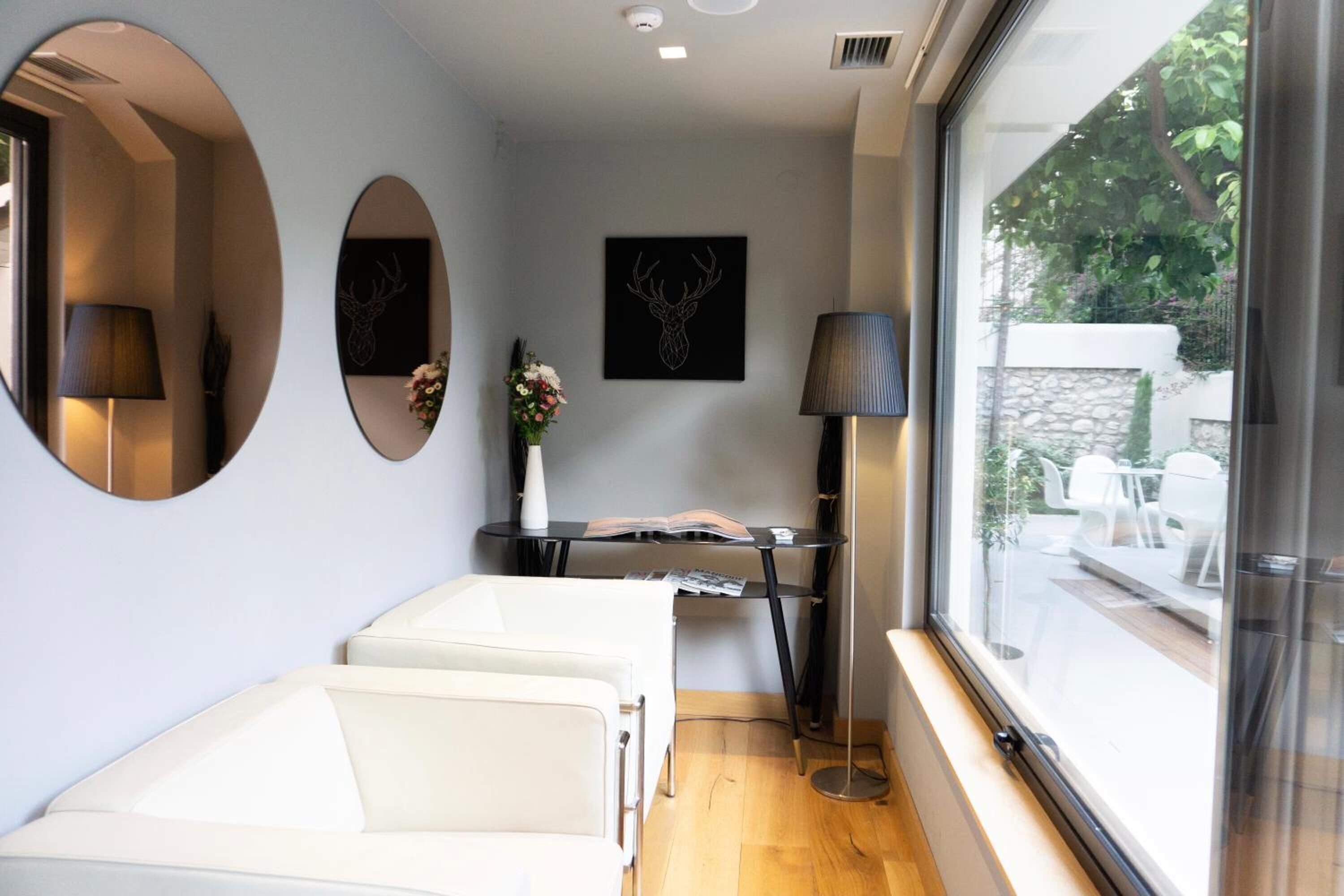 A modern room with a large window, a white sofa, a small table with a book, and two wall-mounted lamps.