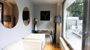 A modern room with a large window, a white sofa, a small table with a book, and two wall-mounted lamps.