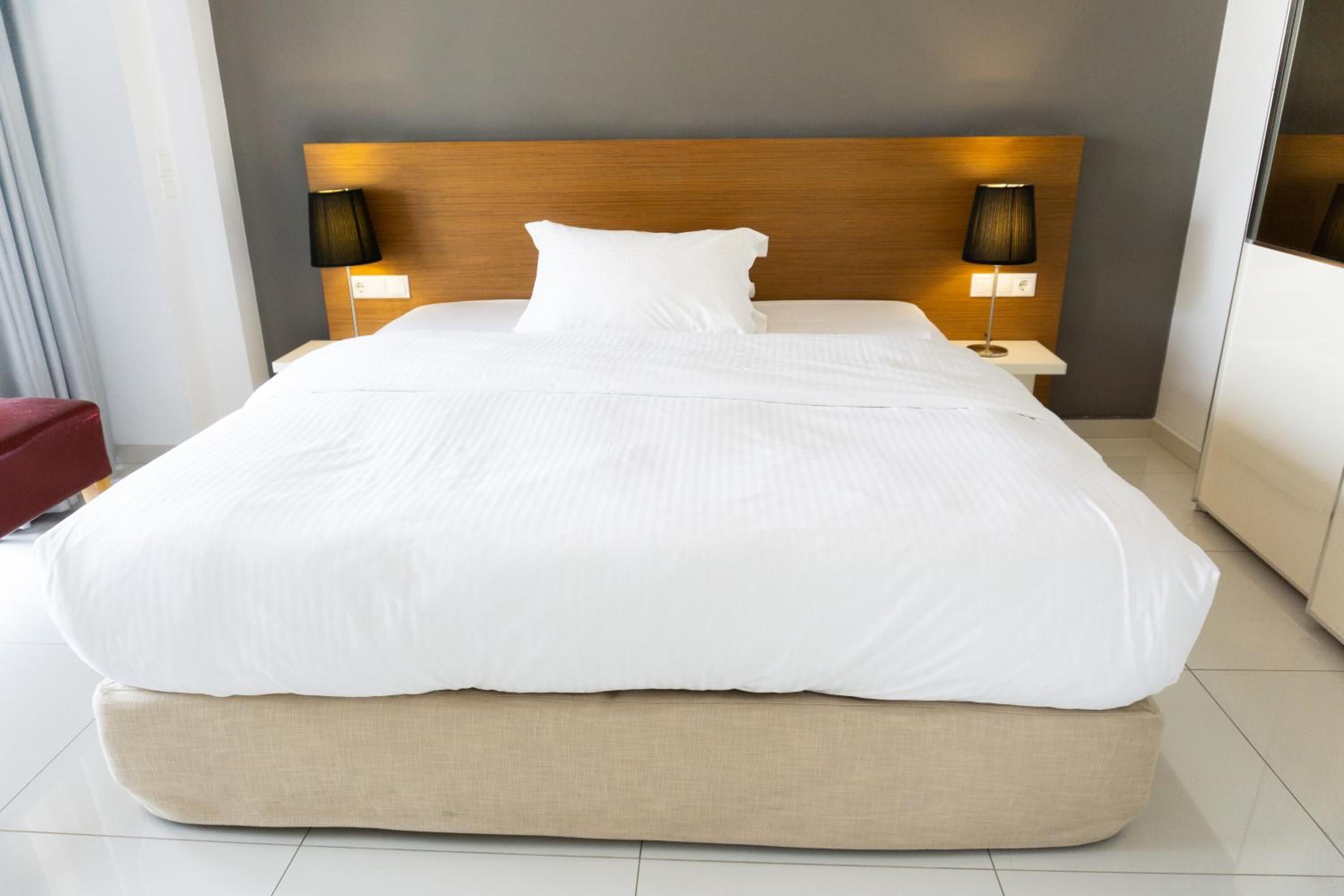 A modern hotel room with a large bed, two bedside lamps, and a wooden headboard.