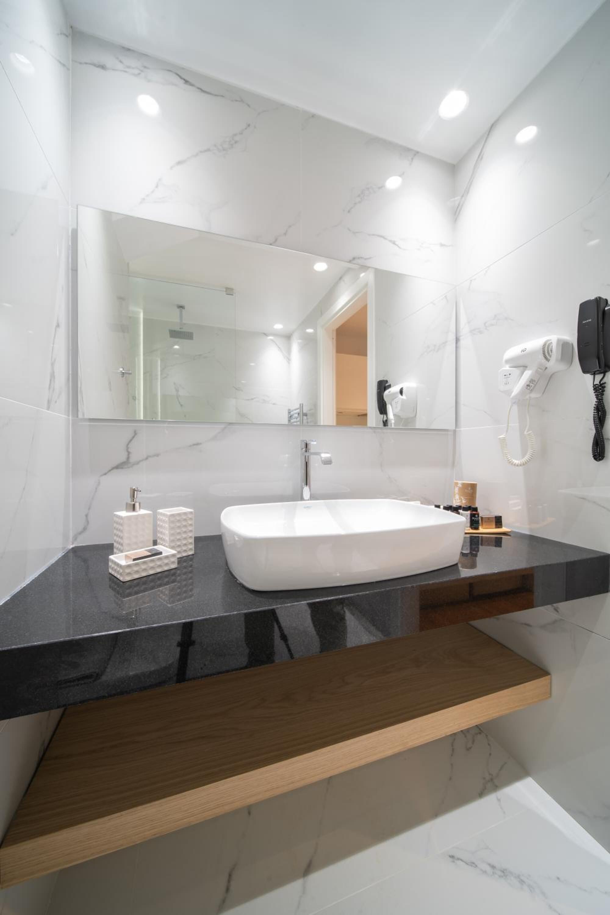 A modern bathroom with a white marble sink, a large mirror, and a hairdryer mounted on the wall.