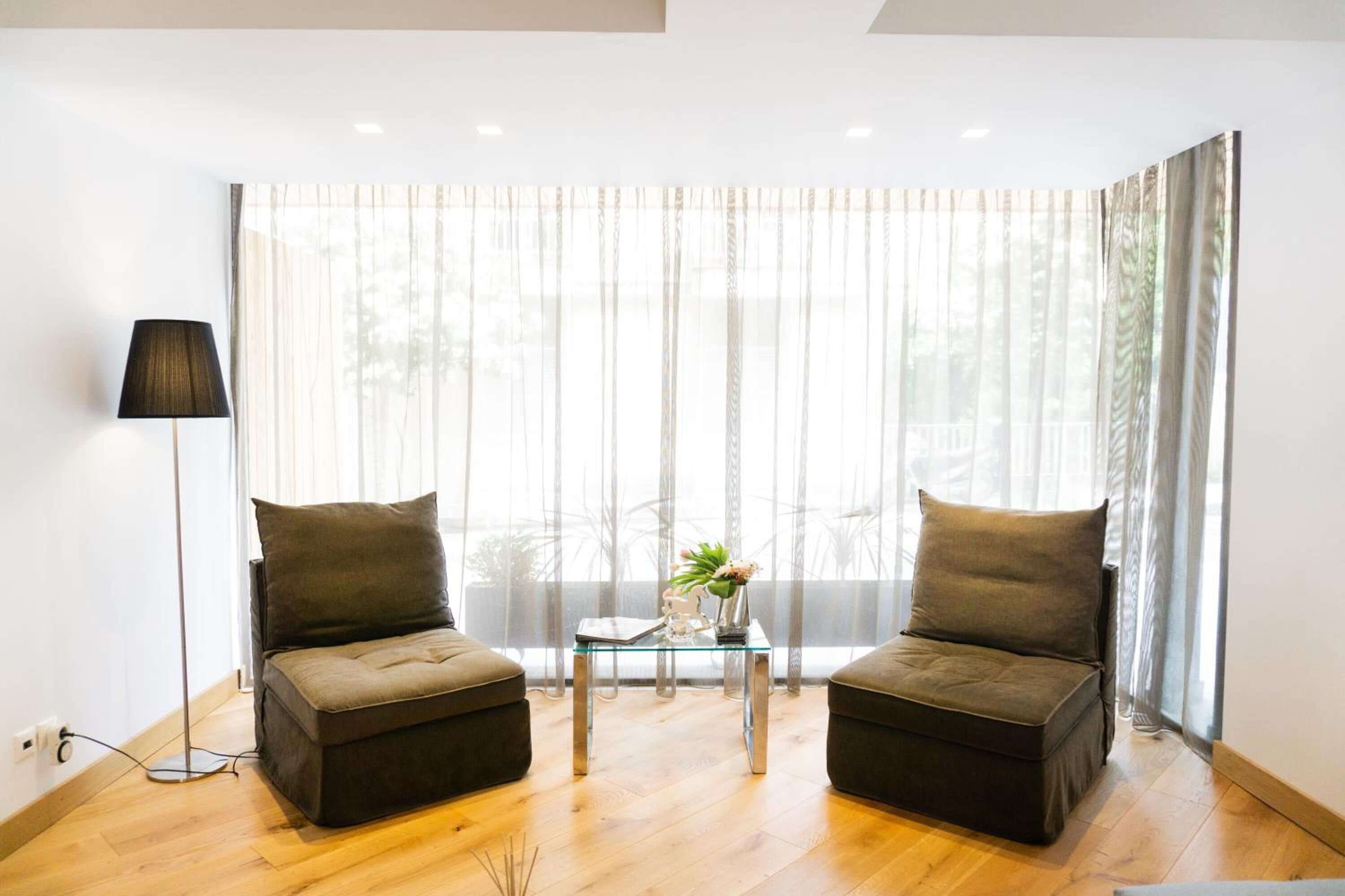 Una sala moderna con dos sillones acolchados, una mesa de centro de vidrio y una lámpara de pie.