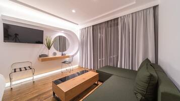A modern living room with a wooden coffee table, a green sofa, a TV mounted on the wall, and a large window with curtains.