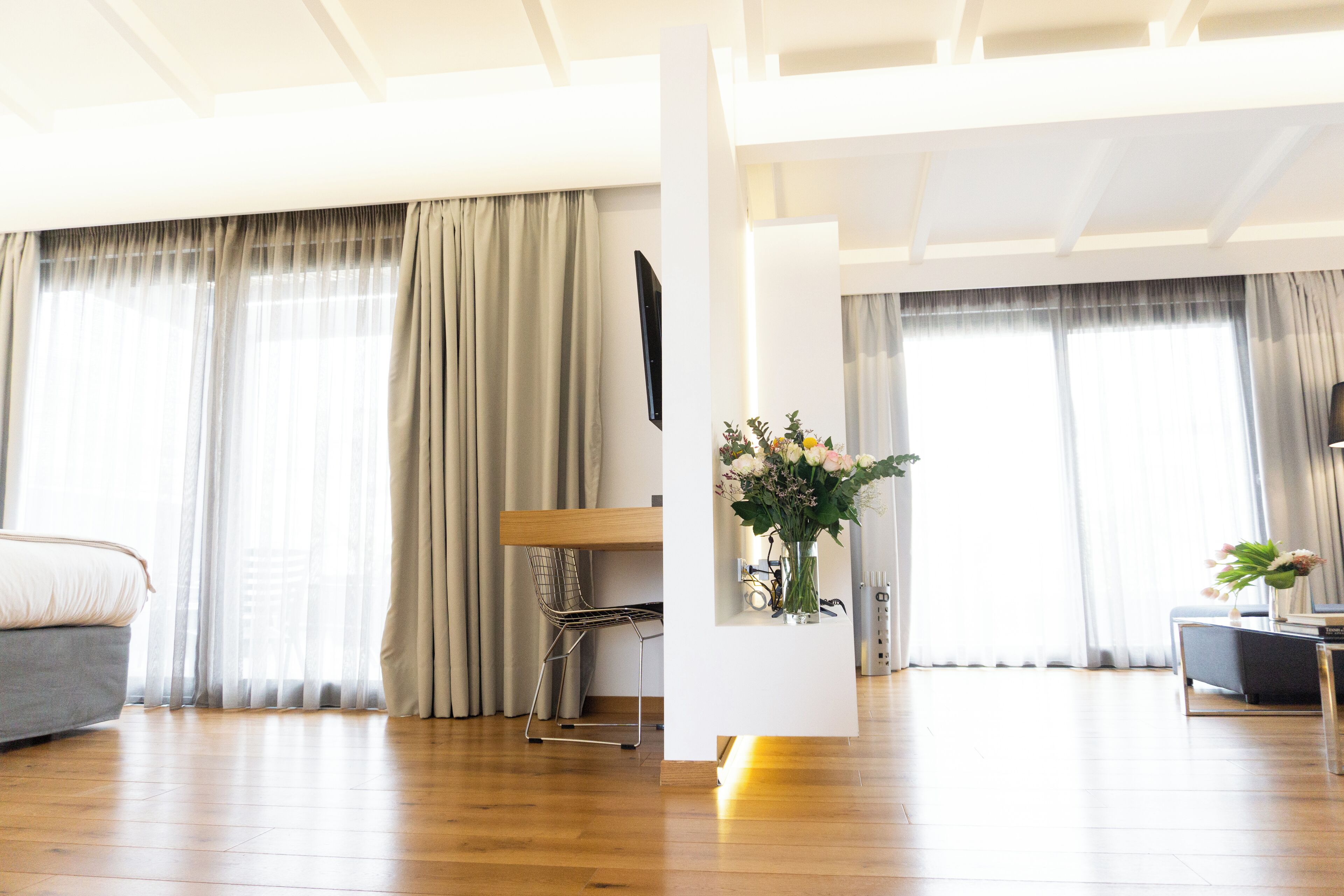 Een moderne woonkamer met een houten vloer, een bank, een eettafel met stoelen, en een decoratieve vaas met bloemen.