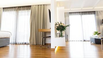 Een moderne woonkamer met een houten vloer, een bank, een eettafel met stoelen, en een decoratieve vaas met bloemen.