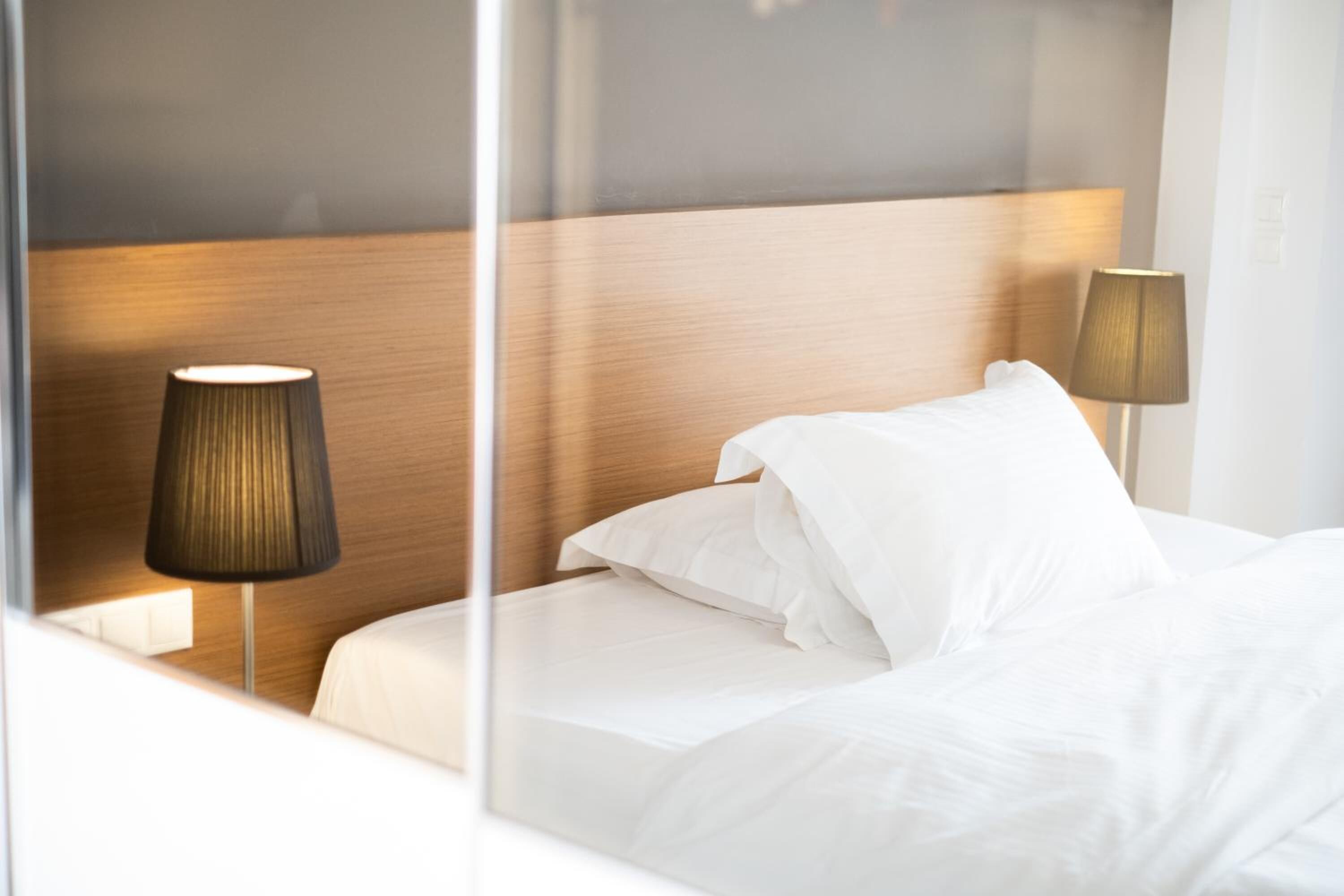 A modern hotel room with a wooden headboard, white bedding, and two bedside lamps.
