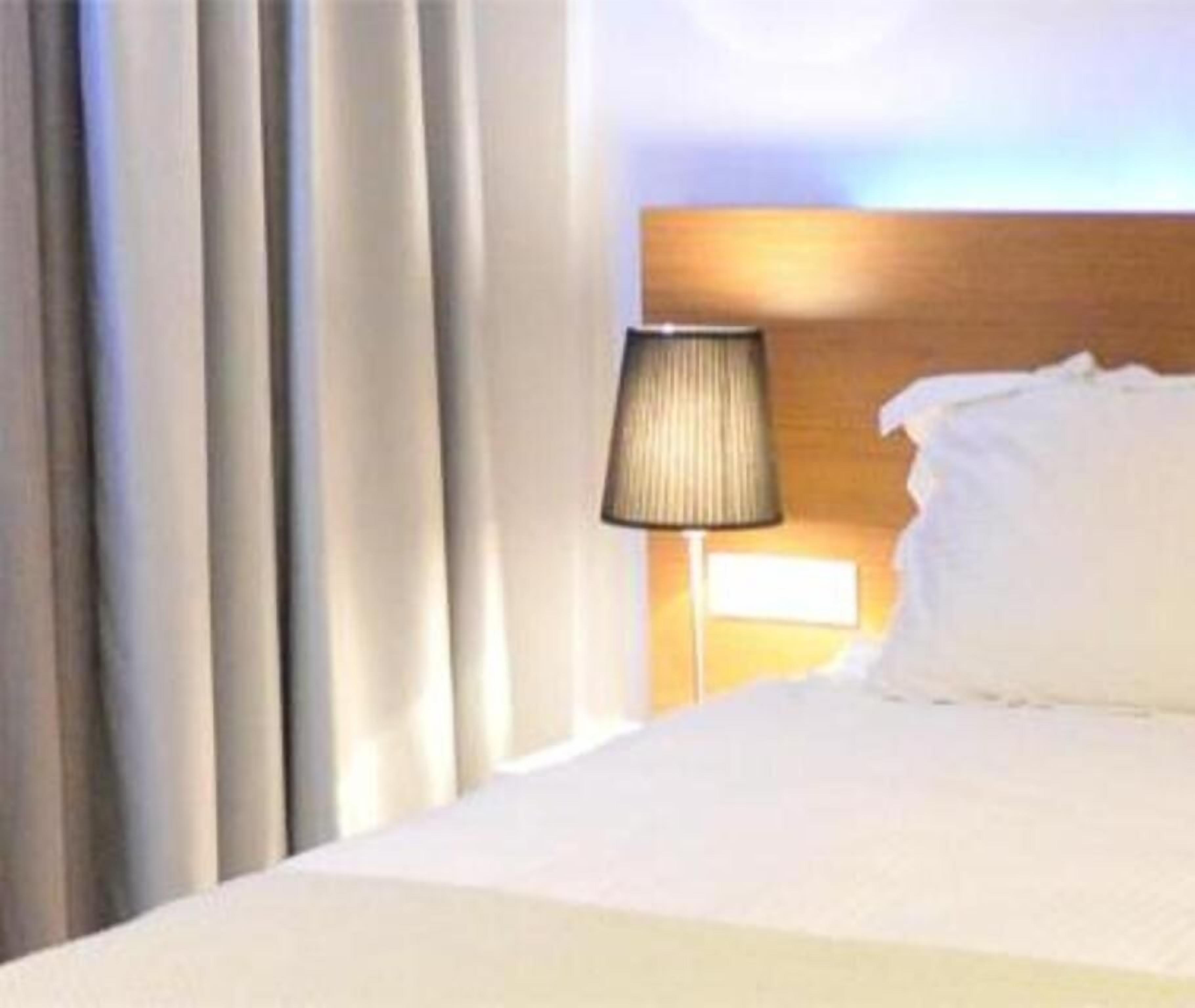 Et hotelværelse med en seng, en lampe og gardiner.