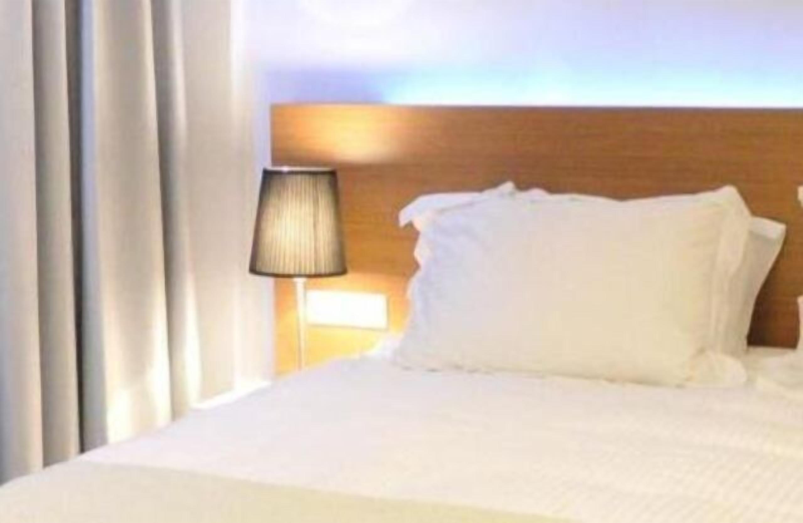 Quarto de hotel com uma cama grande, uma luminária de cabeceira e vista para o céu.
